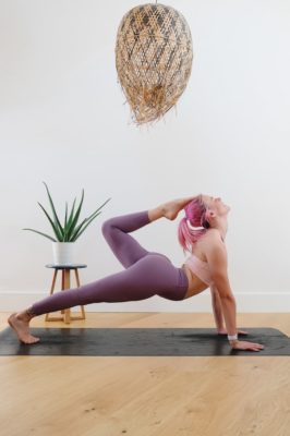 Young woman holds a yoga pose on her yoga mat in her home gym
