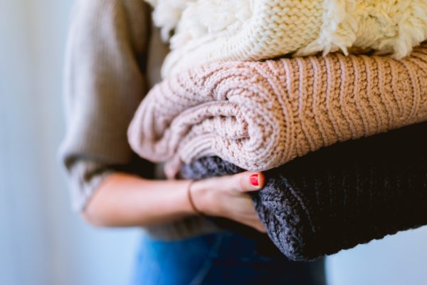 A person holding folded woollen clothes.