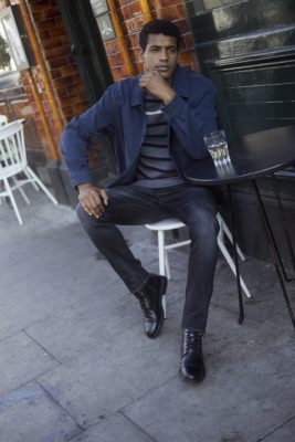 A man in slim-fit jumper and dark wash jeans sitting outside a cafe